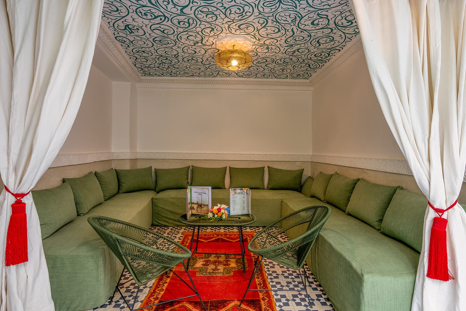 Le salon : banquettes basses vert olive, rideaux de coton blanc retenus par des pompons rouges, plafond peint à la main d'arabesques vertes.